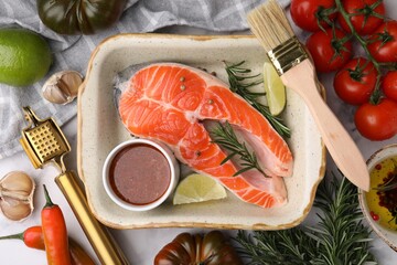 Fresh fish, lime, rosemary and marinade in baking dish surrounded by products on light table, flat...