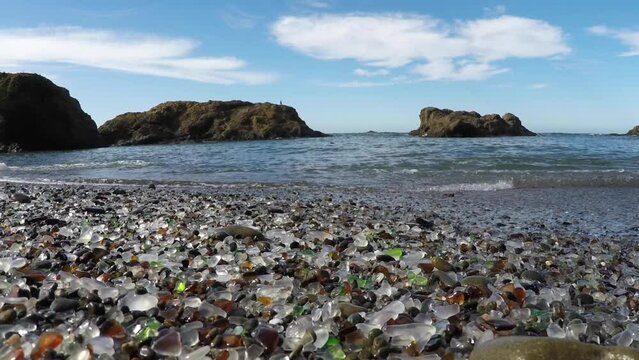 A rocky beach with a large body of water in the background. The beach is covered in broken glass, giving it a somewhat eerie and dangerous appearance