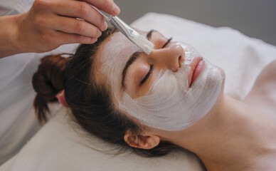 Young woman getting facial care by beautician at spa salon. Face peeling mask, spa beauty...