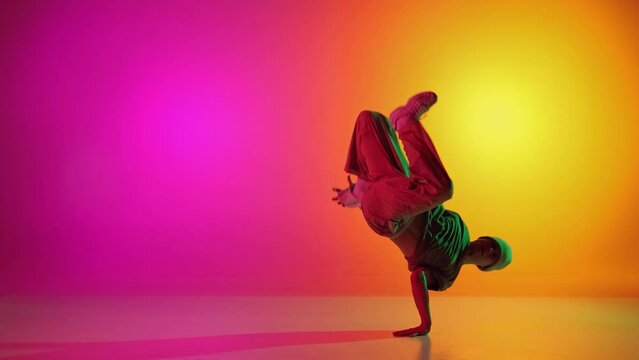Self-expression through moves. Contemporary dancer dancing hip-hop in neon light against gradient pink-yellow background. Concept of art, hobby, sport, creativity, fashion and style, action. Ad
