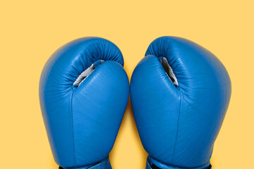 Blue boxing gloves isolated on yellow background close-up. A pair of blue leather boxing gloves top...