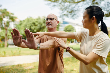 Tai chi instructor explaining g client how to keep arms straight when doing exercise - 786571969