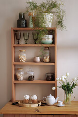 Wooden shelf with various dishes on a white background and a bouquet of tulips. Concept for interior design inspiration and home decoration.