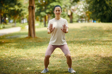 Smiling woman doing tai chi horse stance when breathing out outdoors - 786572582