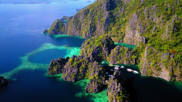 Aerial Tilt Down Shot Of Outriggers Amidst Green Rock Formations, Drone Flying Forward Over Sea On Sunny Day - Palawan, Philippines