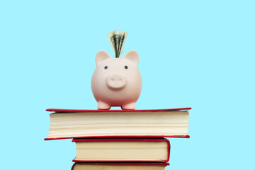 Piggy bank on a composition with hardcover books isolated on blue background. Back to school. copy...