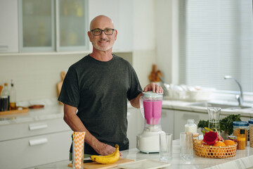 Portrait of smiling mature man making smoothie in the morning - 786576172