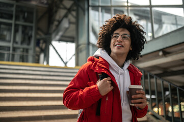 Curly-haired young guy holding a coffee cup and looking excited
