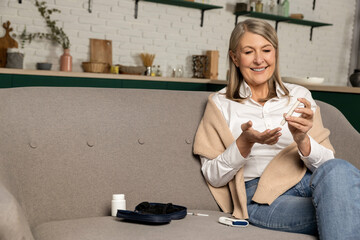 Good-looking mid aged woman sitting on the sofa and making blood sugar test
