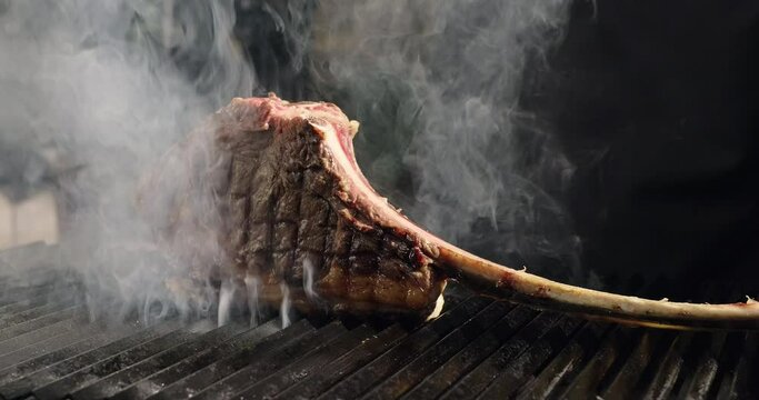Grilling juicy meat steak on barbecue grid. Smoke rising over tomahawk steak