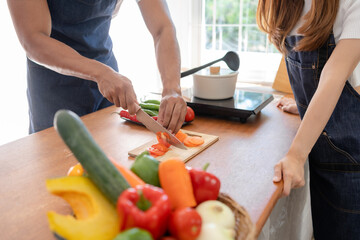 A man and a woman are cooking together in the kitchen. The man is cutting vegetables and the woman...
