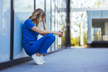 Tired nurse sits on floor outdoors of the medicine clinic after a hard dutty. Exhausted tired...