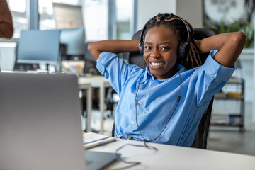 Attractive dark skinned woman in headset working on laptop - obrazy, fototapety, plakaty