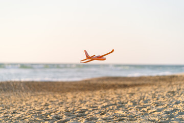A toy airplane glides above the sand against a golden sunset backdrop.