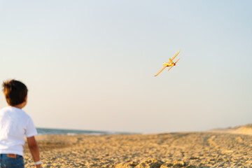 A blurred toy plane in flight above a beach at dusk