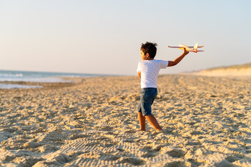 Young boy launching a model plane on a sunny beach