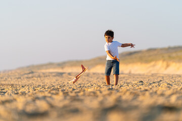 Boy with toy plane prepares for takeoff on beach.