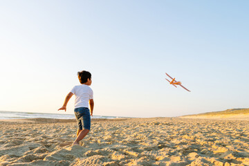Boy in pursuit of a soaring toy airplane on beach