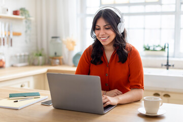 Smiling middle eastern woman with headphones using laptop