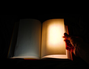 A person's hand opening a book as the page is brightly lit , signifying adventure, learning or the unknown - 786592782