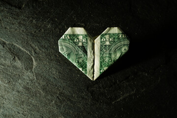 Dollar bill origami heart shape on dark textured background - 786592964