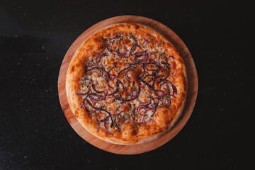 Overhead view of a pizza with purple onion on top of a black granite table.