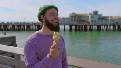Young good-looking African American with thick beard, pair of dreadlocks seen from hat laughing out loud standing on pier on a beautiful sunny day in harbour in Santa Barbara. High quality 4k footage - Powered by Adobe
