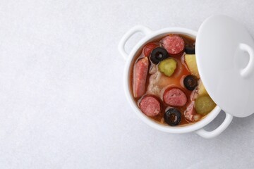 Meat solyanka soup with thin dry smoked sausages in pot on light table, top view. Space for text