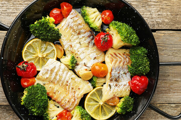Tasty cod cooked with vegetables in frying pan on wooden table, top view - obrazy, fototapety, plakaty