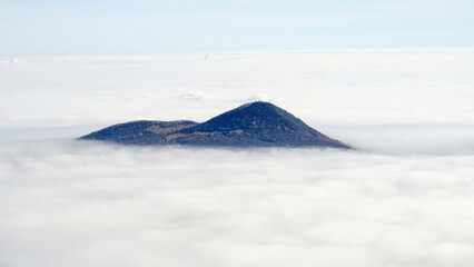 A lone mountain peak emerges above a dense sea of clouds under a clear sky