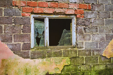 A shattered window in a decaying cinder block structure tells tales of neglect and abandonment