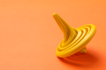 One yellow spinning top on orange background, closeup. Space for text