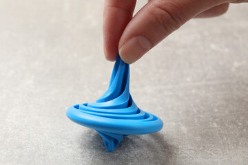 Woman playing with blue spinning top at grey textured background, closeup