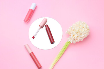 Different lip glosses, hyacinth and mirror on pink background, flat lay