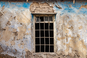 Fototapeta na wymiar Weathered blue wall with barred window. Vintage window on peeling blue.