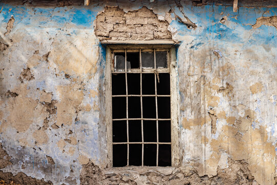 Weathered blue wall with barred window. Vintage window on peeling blue.