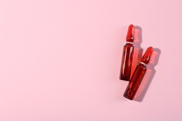 Glass ampoules with liquid on pink background, top view. Space for text