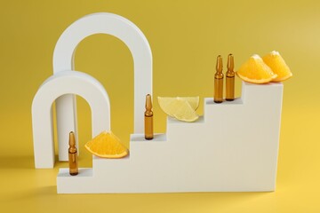Stylish presentation of skincare ampoules with vitamin C and citrus slices on yellow background