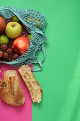 String bag with fresh fruits and pieces of bread on color background, flat lay. Space for text