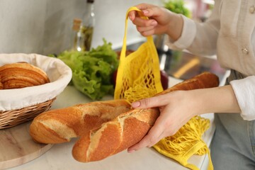 Woman taking baguette out from string bag at countertop, closeup
