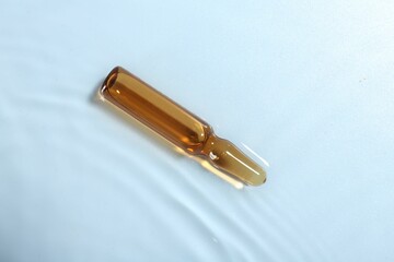 Skincare ampoule in water on light blue background, top view