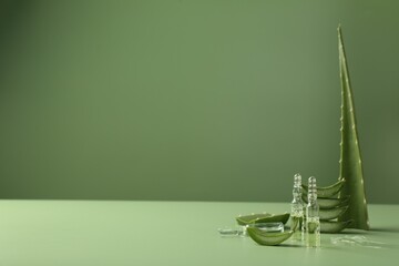 Skincare ampoules with extract of aloe vera and cut green leaves on color background. Space for text