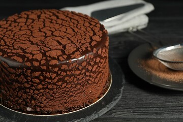 Delicious chocolate truffle cake and cocoa powder on black wooden table, closeup