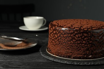 Delicious chocolate truffle cake and cocoa powder on black wooden table