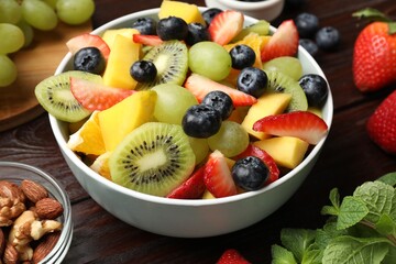 Tasty fruit salad in bowl and ingredients on wooden table, closeup