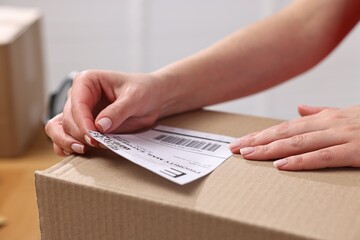 Parcel packing. Post office worker sticking barcode on box indoors, closeup