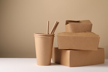 Eco friendly food packaging. Paper containers and straws on white table against beige background, space for text
