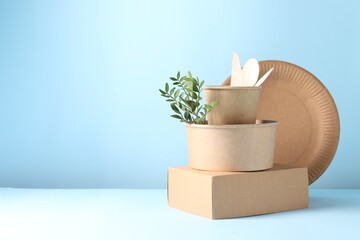 Eco friendly food packaging. Paper containers, tableware and green twig on white table against light blue background, space for text