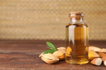 Almond oil in bottle, nuts and leaves on wooden table, closeup. Space for text
