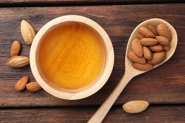 Almond oil in bowl, nuts and spoon on wooden table, flat lay